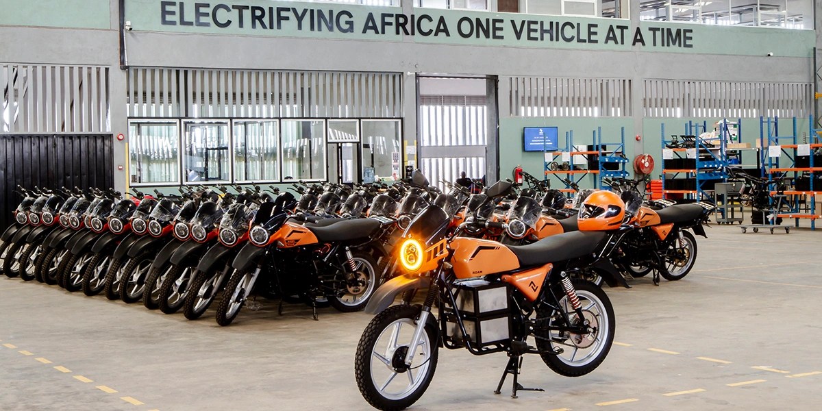 Roam motocycles lined up in 100's Sign saying "Electrifying Africa one vehicle at a time"