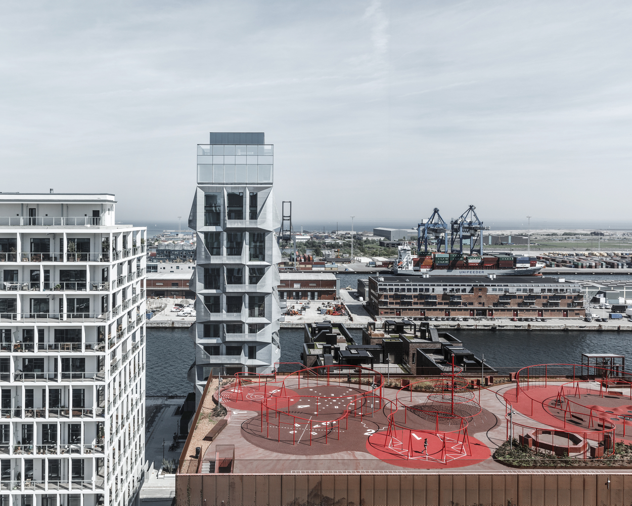 Old brutalist grain Silo in Copenhagen. Freshly clad and repurposed as an office building with grey metal panels. A rooftop playground in the foreground.