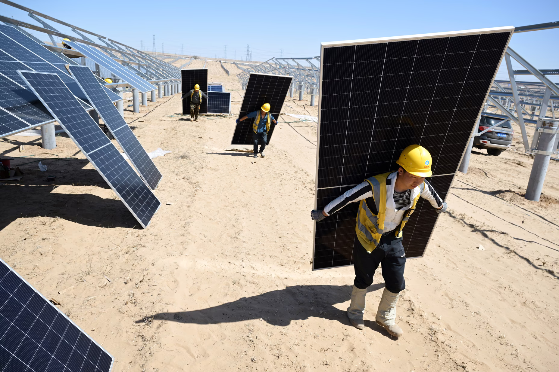 Workers carry solar panels to be installed in the desert at the Ningguoyun Lingwu 1-million-kilowatt photovoltaic project in Lingwu, in China's northern Ningxia Hui Autonomous Region, on April 14, 2025. Image Via: AFP / Getty